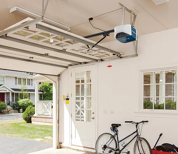 Open garage showing a neatly organized space with a parked bicycle, a closed white door leading outside, bright lighting, and a view of a suburban street.