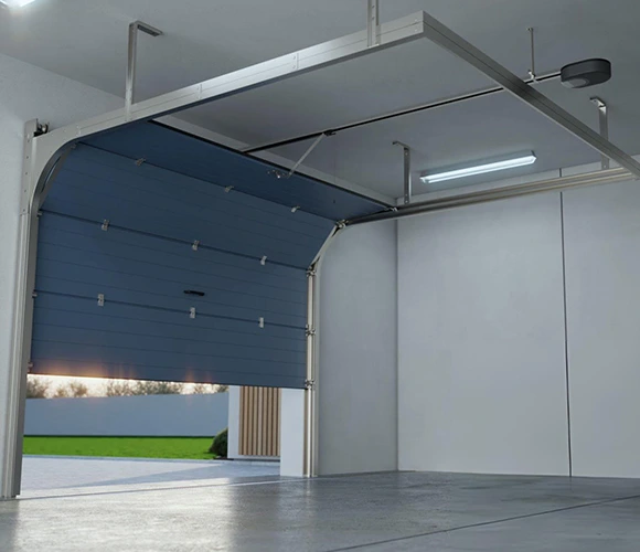 Open garage with a raised blue sectional door, sleek concrete floor, and modern lighting. Outside, a manicured lawn and a sunset sky are visible.