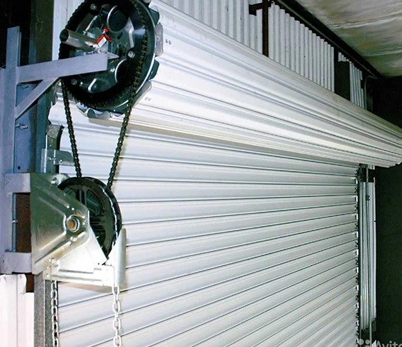 Close-up of a white metal roll-up garage door with a chain hoist mechanism. The image conveys industrial functionality and efficiency.